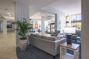 A modern lobby with a sofa, chairs, a potted plant, and a sign. - Fully Renovated Condo on Bay | Resort Amenities (Siesta Key)