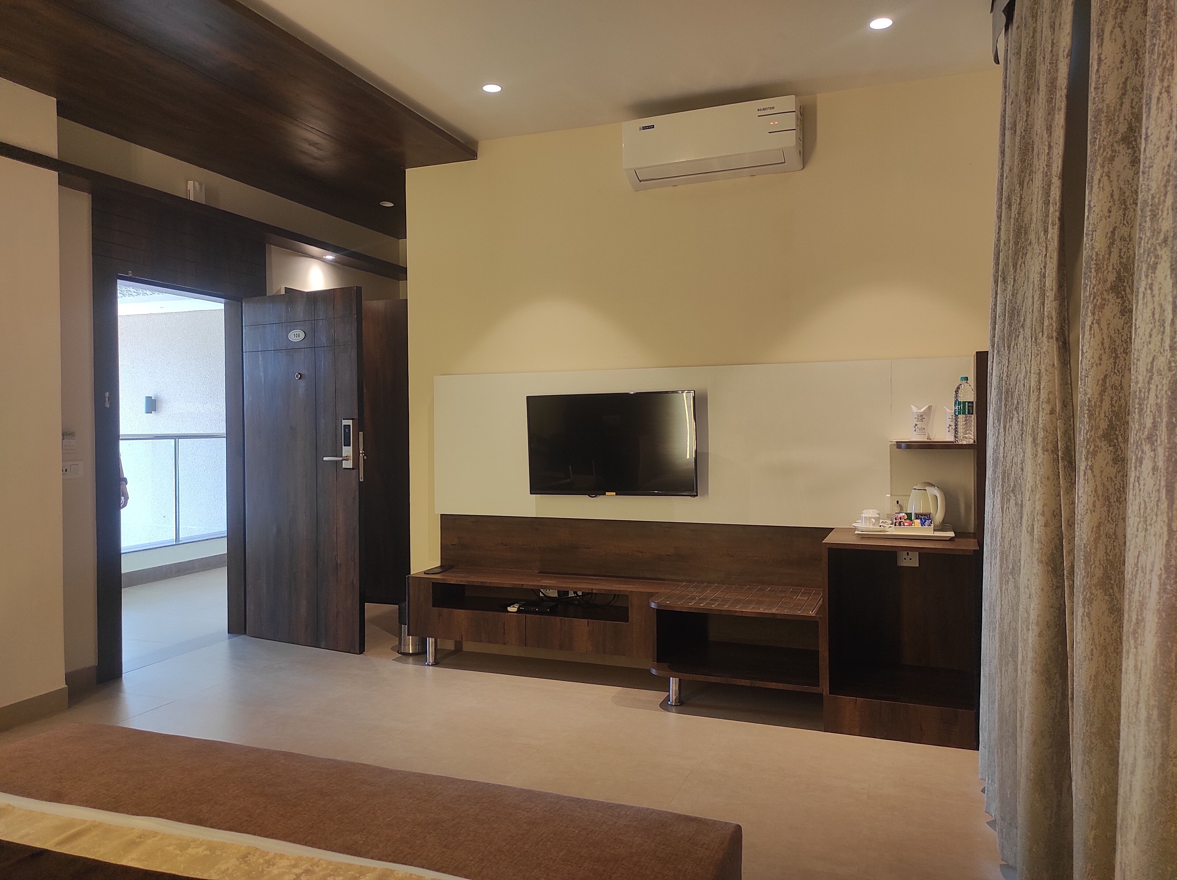 Habitació d'hotel moderna amb un gran televisor de pantalla plana penjat a la paret, una banca de fusta i una taula petita amb un bullidor i tasses.