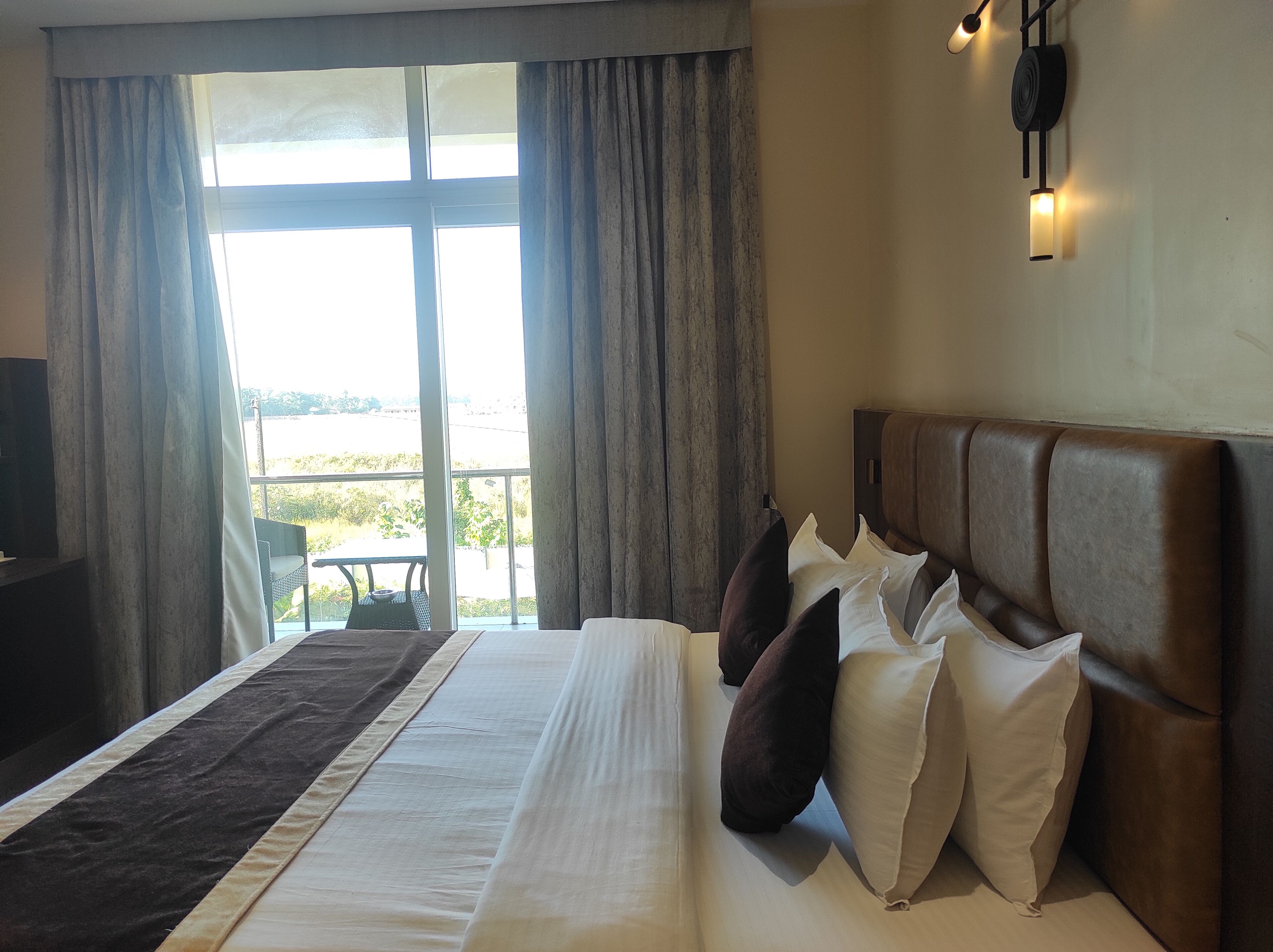 A hotel room with a large bed, a view of the outdoors, and a television on a stand.