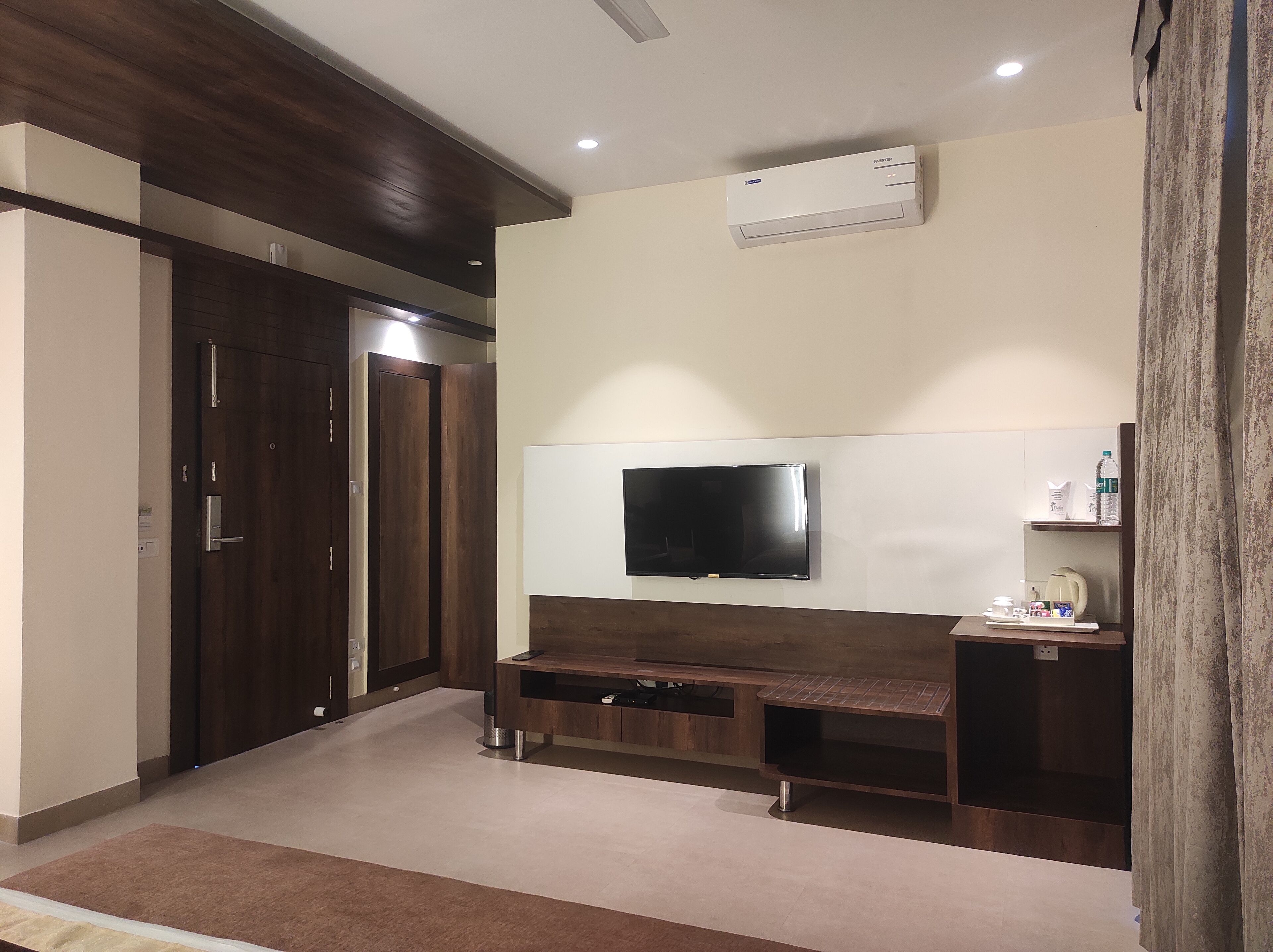 Ein modernes Hotelzimmer mit flachbildfernseher an der Wand, einer Holz-Unterhaltungseinrichtung, einem Schrank mit Spiegel und einer Klimaanlage.