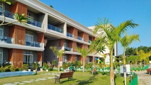 Un hotel de varios pisos con balcones, un césped bien cuidado y palmeras.