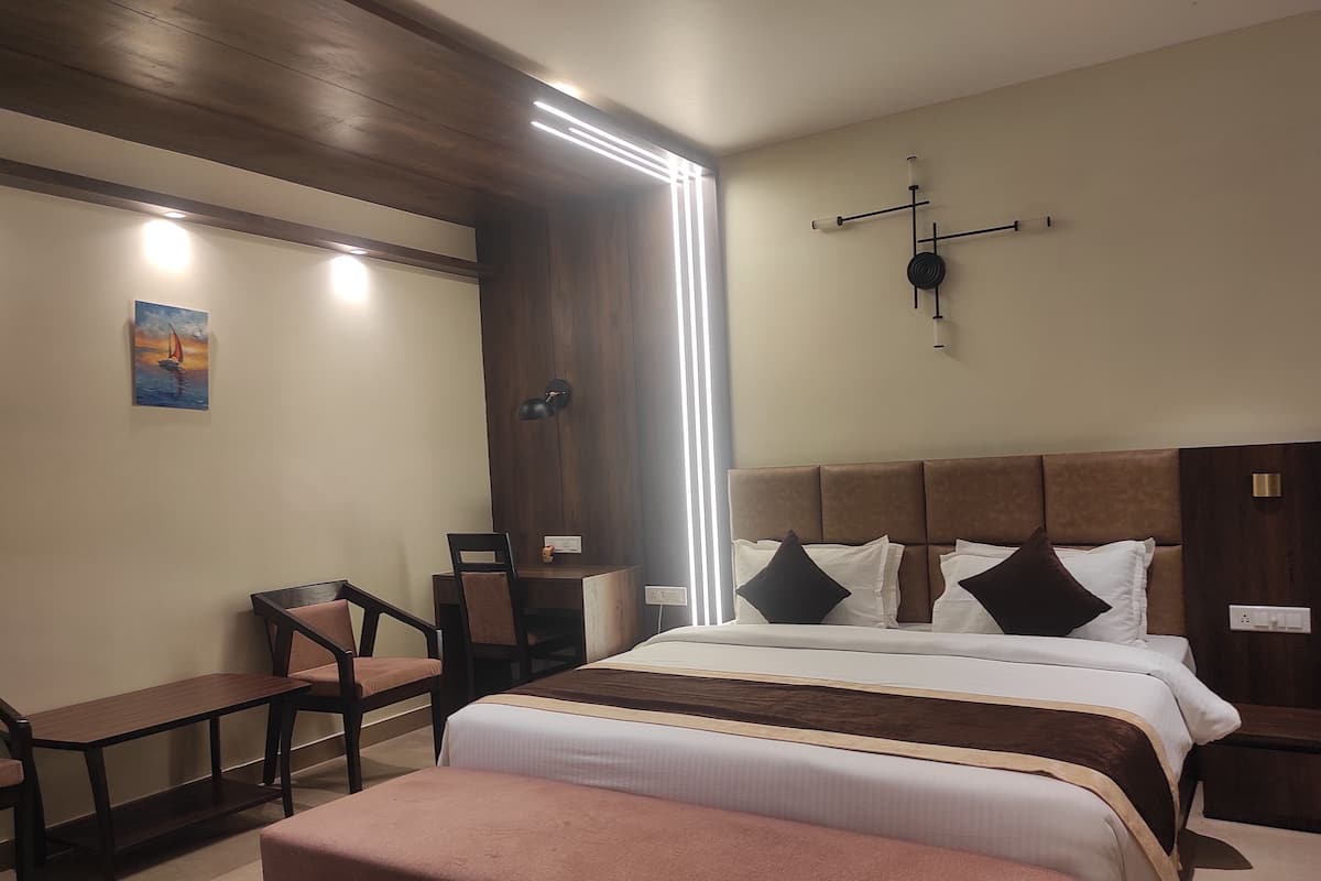 Hotellihuoneessa on suuri sänky, työpöytä ja tuoli. Seinällä on taulu ja toisella seinällä kello.