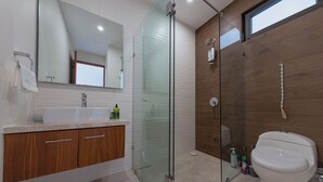 A modern bathroom with a glass-enclosed shower, a white sink, wooden cabinets, and a toilet.