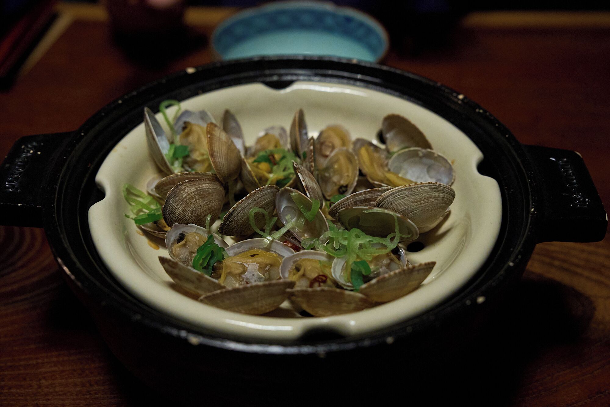 A dish of clams in a black pot on a table.