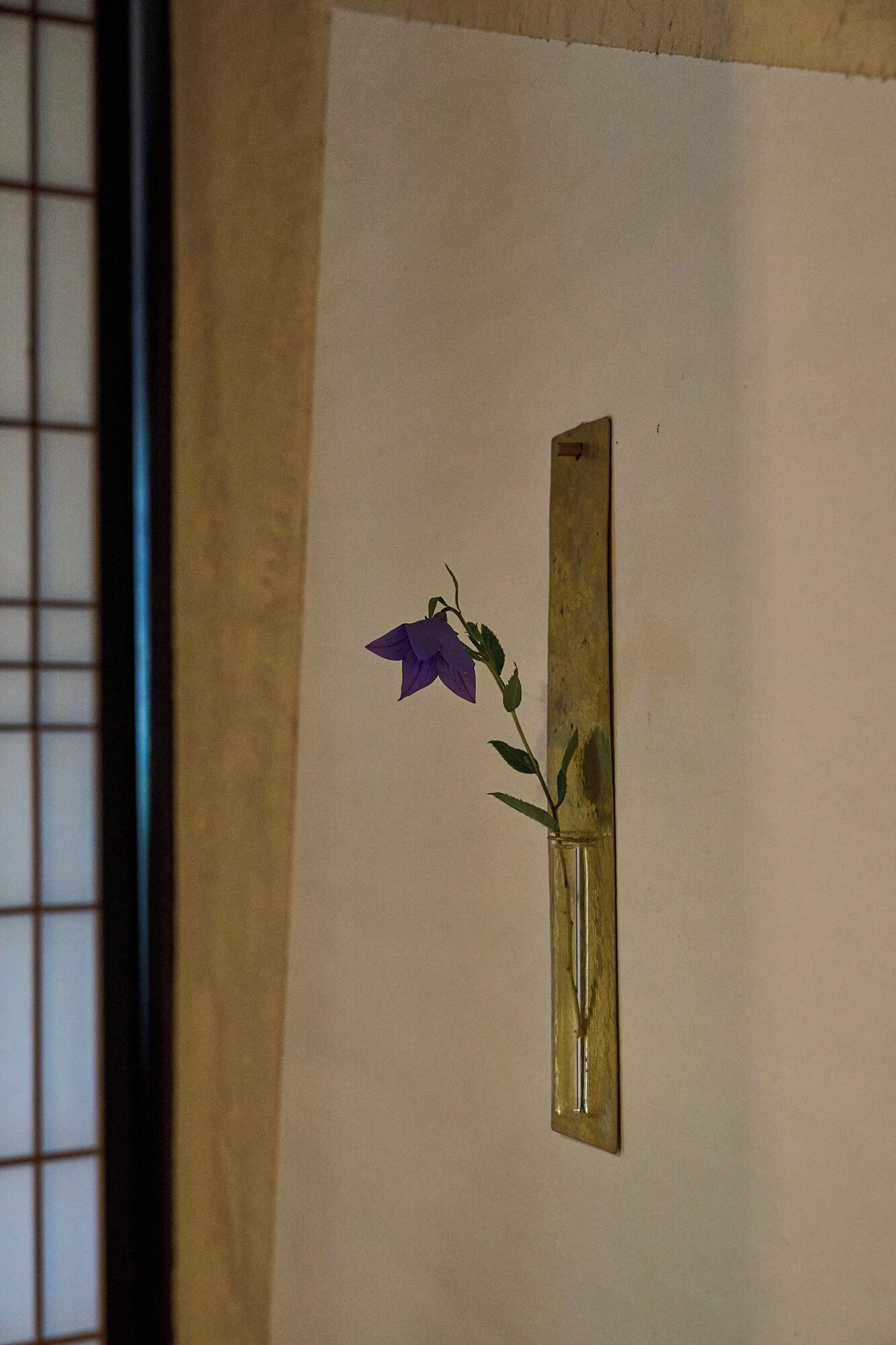 A framed artwork of a purple flower in a glass vase on a beige wall.