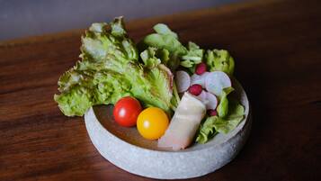 A salad with lettuce, radishes, a tomato, and a cheese slice on a round stone plate.