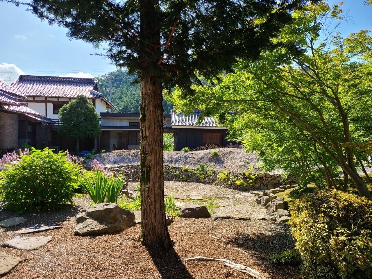 A traditional Japanese building with a tiled roof, surrounded by a garden with rocks, trees, and shrubs.