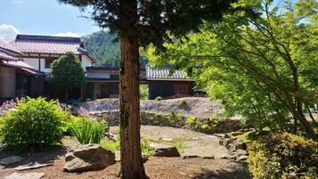 A traditional Japanese building with a tiled roof, surrounded by a garden with rocks, trees, and shrubs.