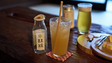 Un verre de jus de pomme avec une paille, une bouteille de jus de pomme et un verre contenant une autre boisson, le tout posé sur une table en bois.