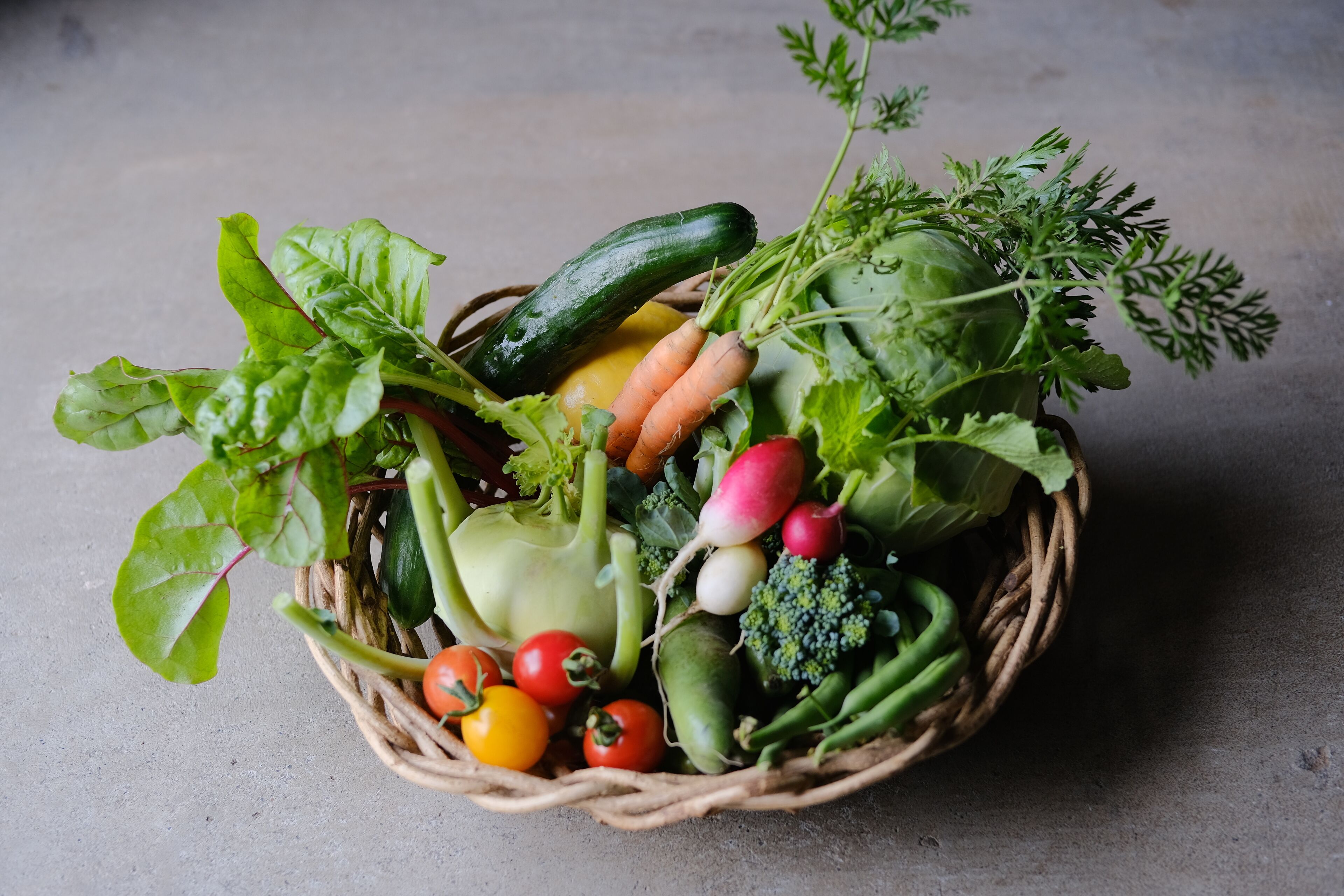 Una cesta repleta de verduras frescas como lechuga, zanahorias, tomates y pepinos.