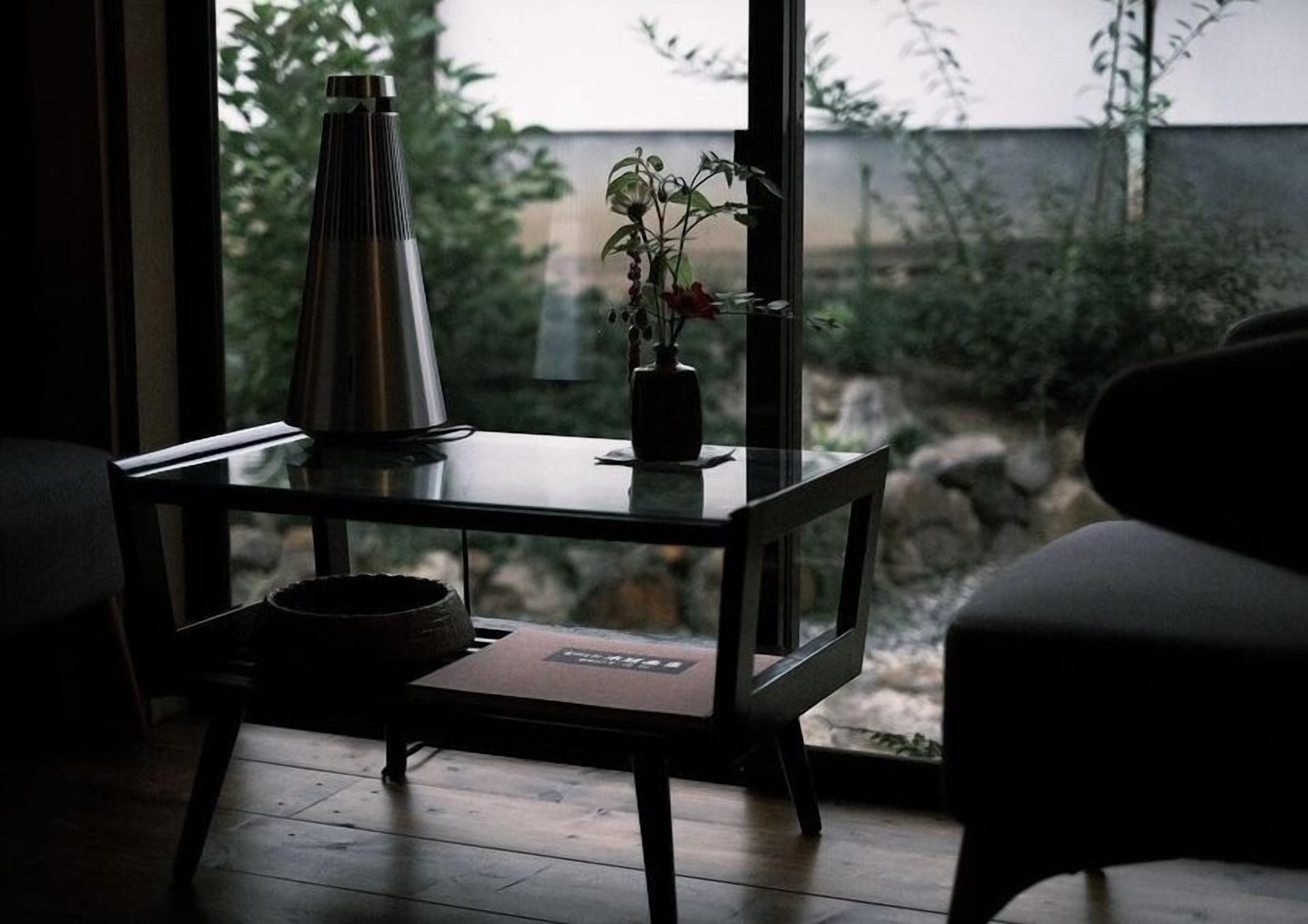 Una habitación moderna con una mesa de vidrio, un jarrón de metal y una planta en maceta.