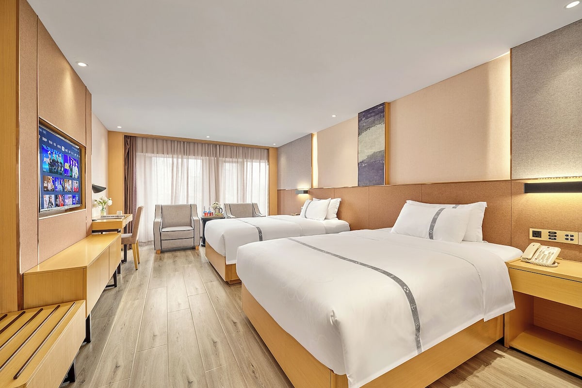 A hotel room with two beds, a desk, a chair, a TV, and a phone.
