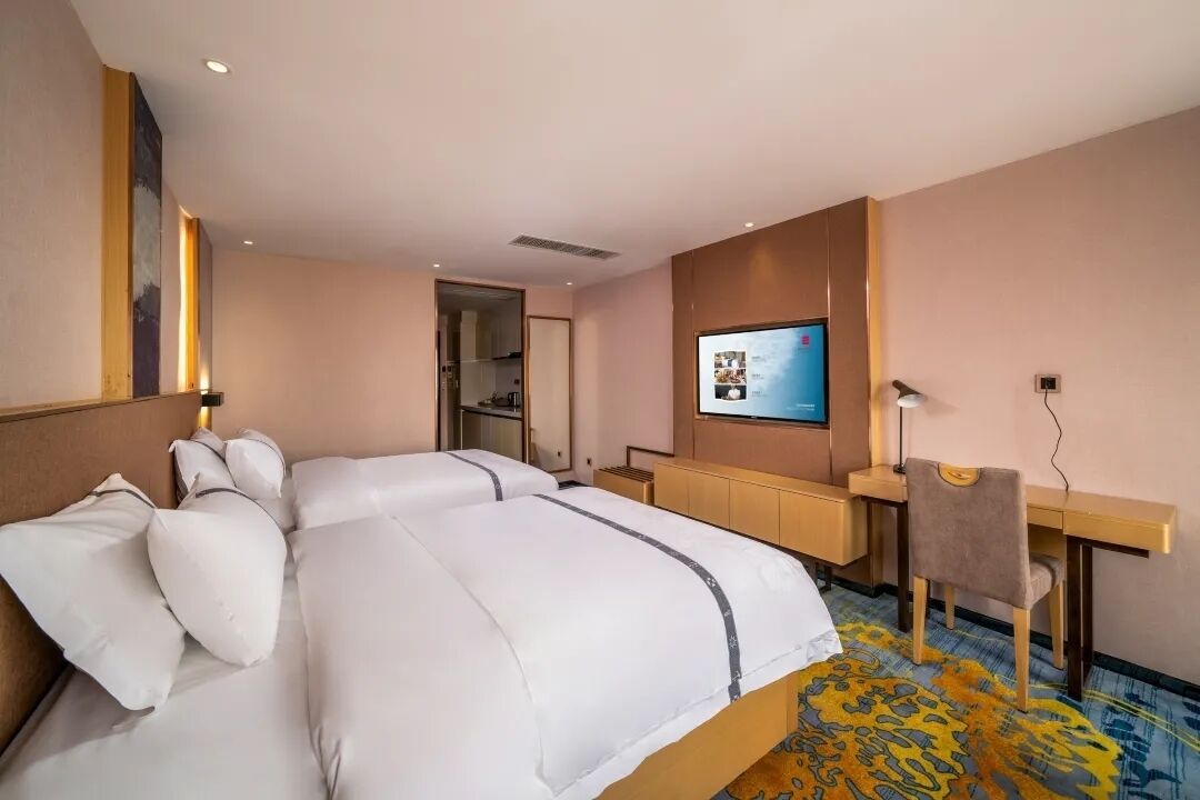 Habitación de hotel con una cama grande, un escritorio, una silla, un televisor y un baño visible a través de una puerta abierta.