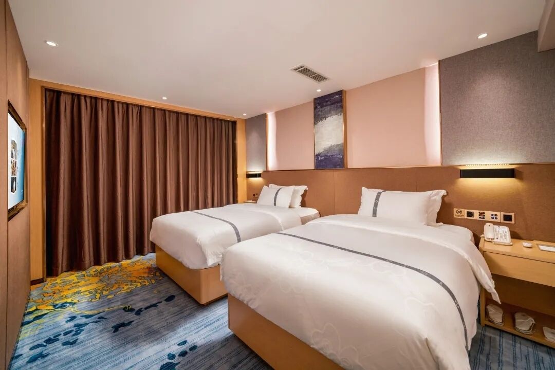 A hotel room with two beds, a large window with curtains, a wall-mounted phone, and a carpeted floor.