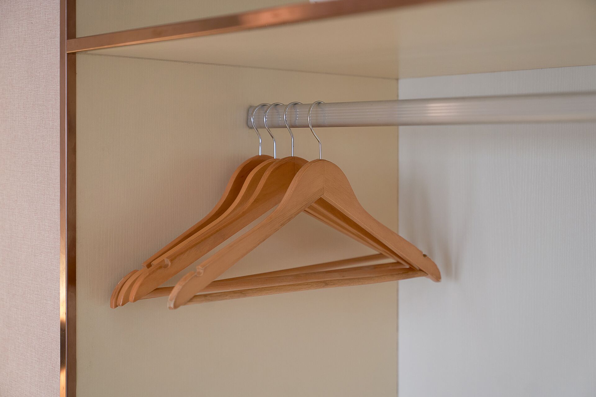 Een houten kledingrek met twee hangers tegen een beige muur.