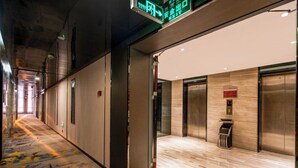 A hotel corridor with an elevator, a trash bin, and a digital sign indicating directions. - YISHANG HOTEL (Guangzhou)