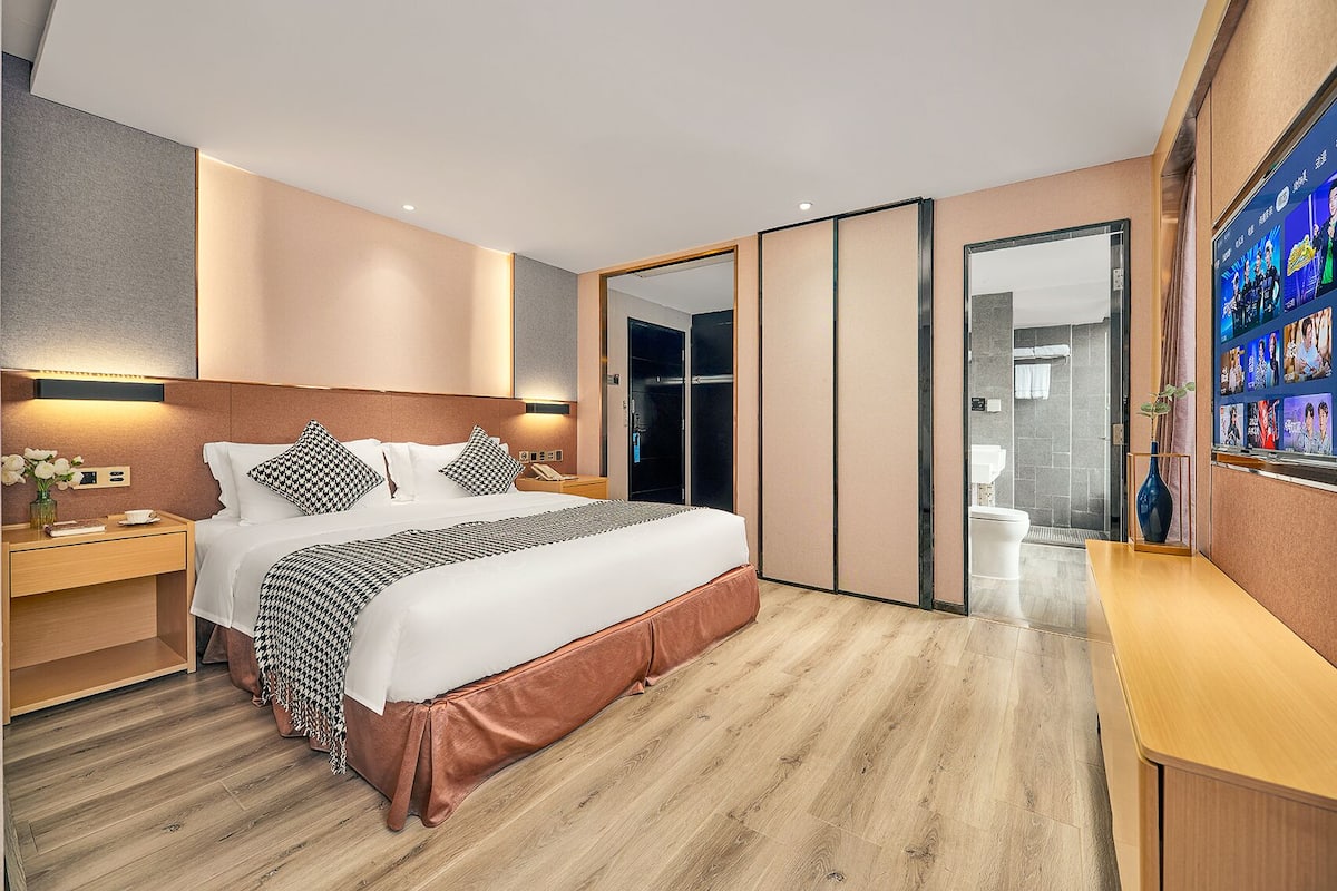 A modern hotel room with a large bed, bedside tables, a mirror, and a TV screen displaying images.