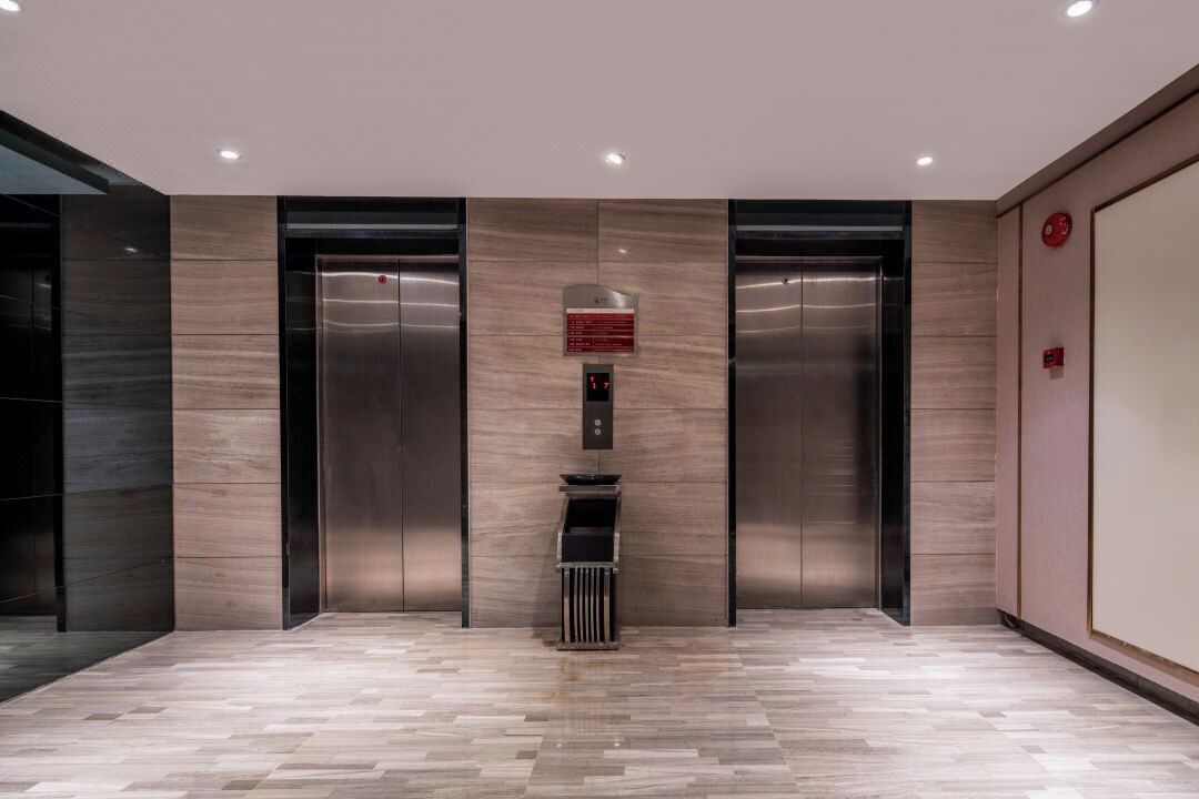 A modern elevator area with a wood-patterned wall, two elevators, and a trash bin.