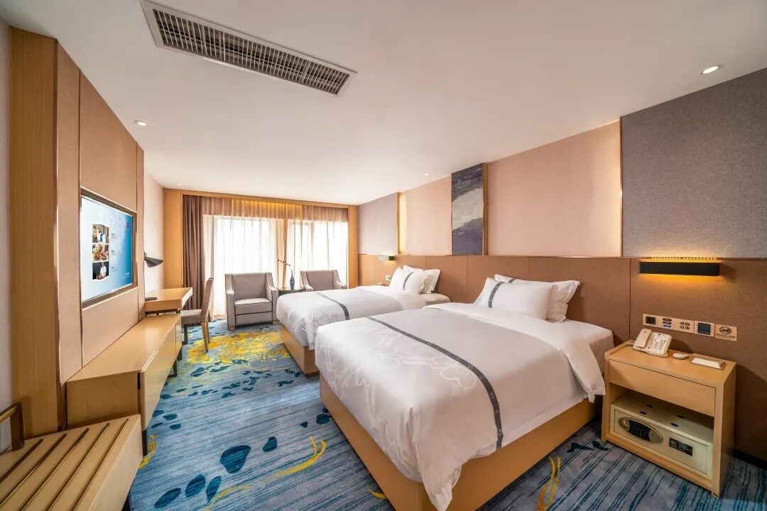 A hotel room with two beds, a desk, a chair, a TV, and a minibar.