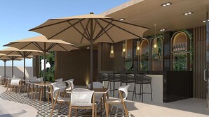 Un área de estar al aire libre con mesas y sillas, grandes sombrillas y una zona de bar con taburetes.