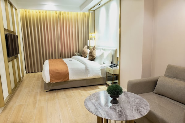 A hotel room with a bed, a bedside table with a lamp, a sofa, and a small round table with a plant. - UMA Hotel and Residences (Naga)
