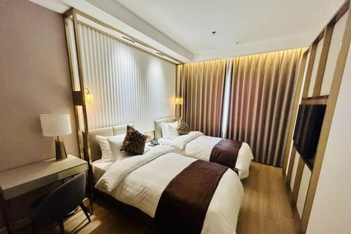A hotel room with two beds, a desk, and a TV.