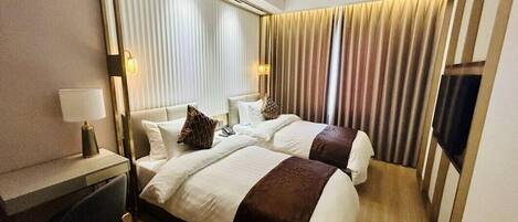 A hotel room with two beds, a desk, and a TV.