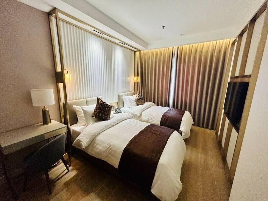 Quarto de hotel com duas camas, uma escrivaninha e uma televisão.