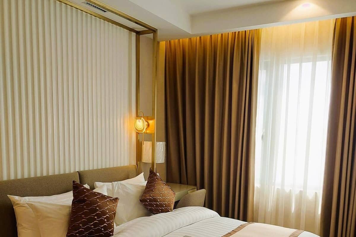 A hotel room with a large bed, a bedside table, a lamp, and a window with curtains.