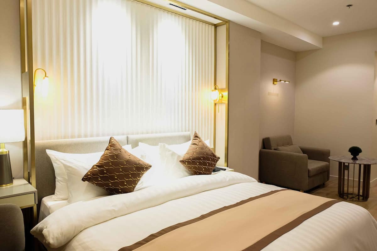 A hotel room with a large bed, a chair, a small table, and a lamp.