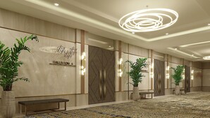 Un moderno vestíbulo de hotel con un mostrador de recepción de mármol, un cartel que indica 'Ballroom A' y una alfombra estampada.