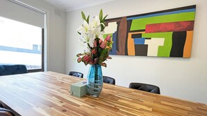 Et mødelokale med et træbord, en vase med blomster, et billede på væggen og et vindue med persienner.