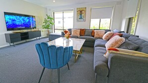 En moderne stue med et fladskærms-tv, en sofa, et sofabord og en blå lænestol.