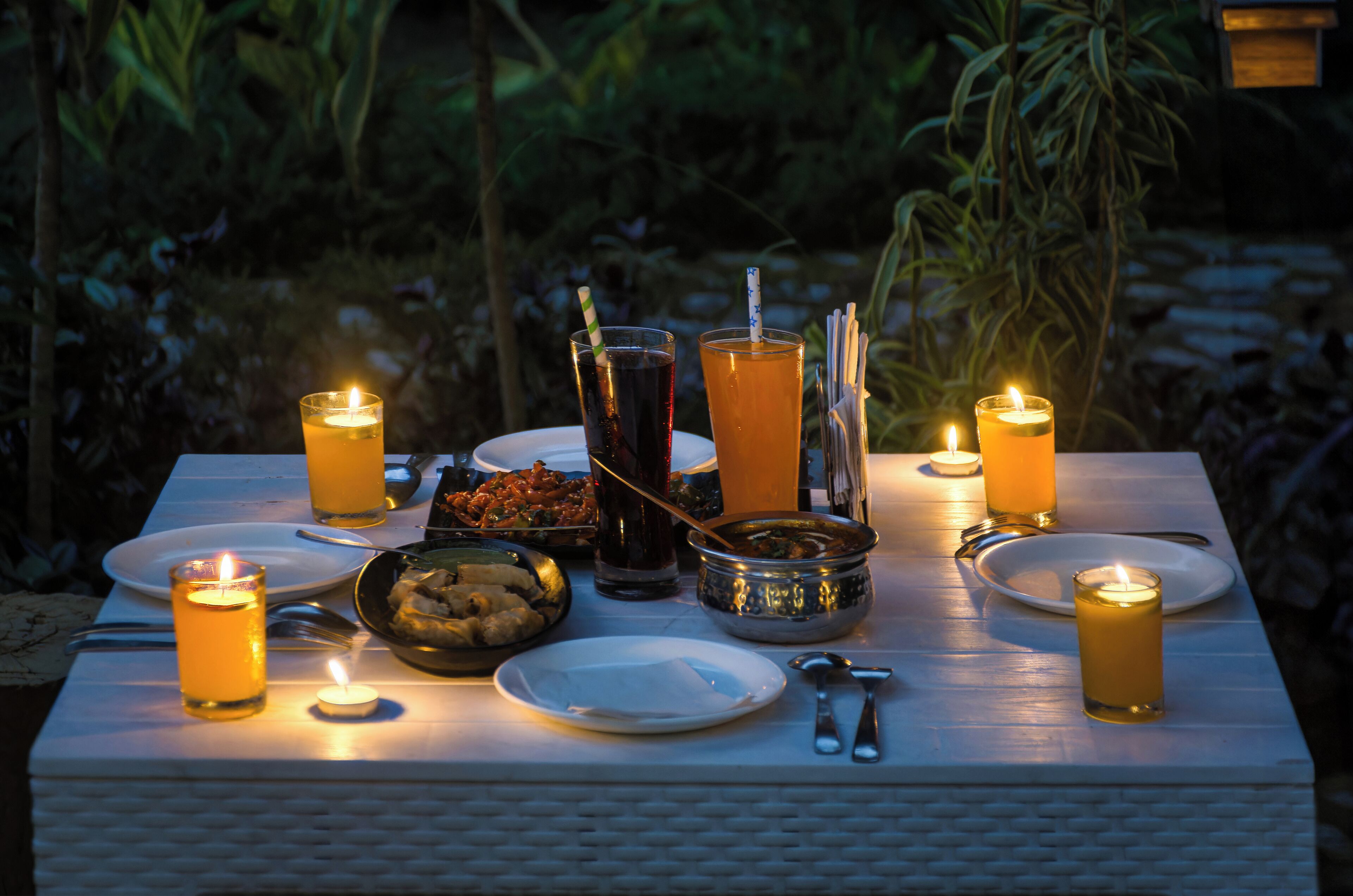 A table set for a meal with candles, plates, cutlery, and a drink.