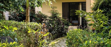 A stone pathway leading to a building with a balcony, surrounded by lush greenery.