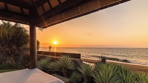 Vista a la playa desde un espacio cubierto con barandilla, con vista al océano al atardecer.