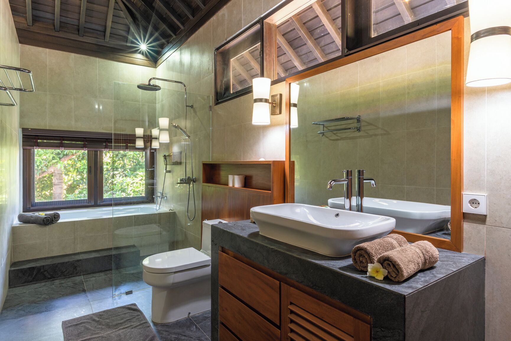 A modern bathroom with a glass-enclosed shower, a freestanding bathtub, a vanity with a large mirror, and a toilet.