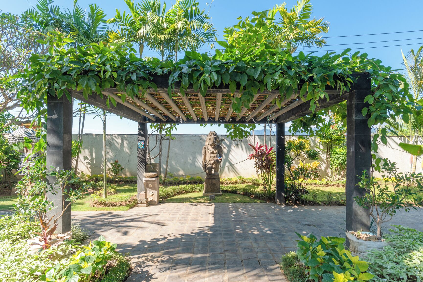 A covered garden area with a statue, stone pillars, and lush greenery.