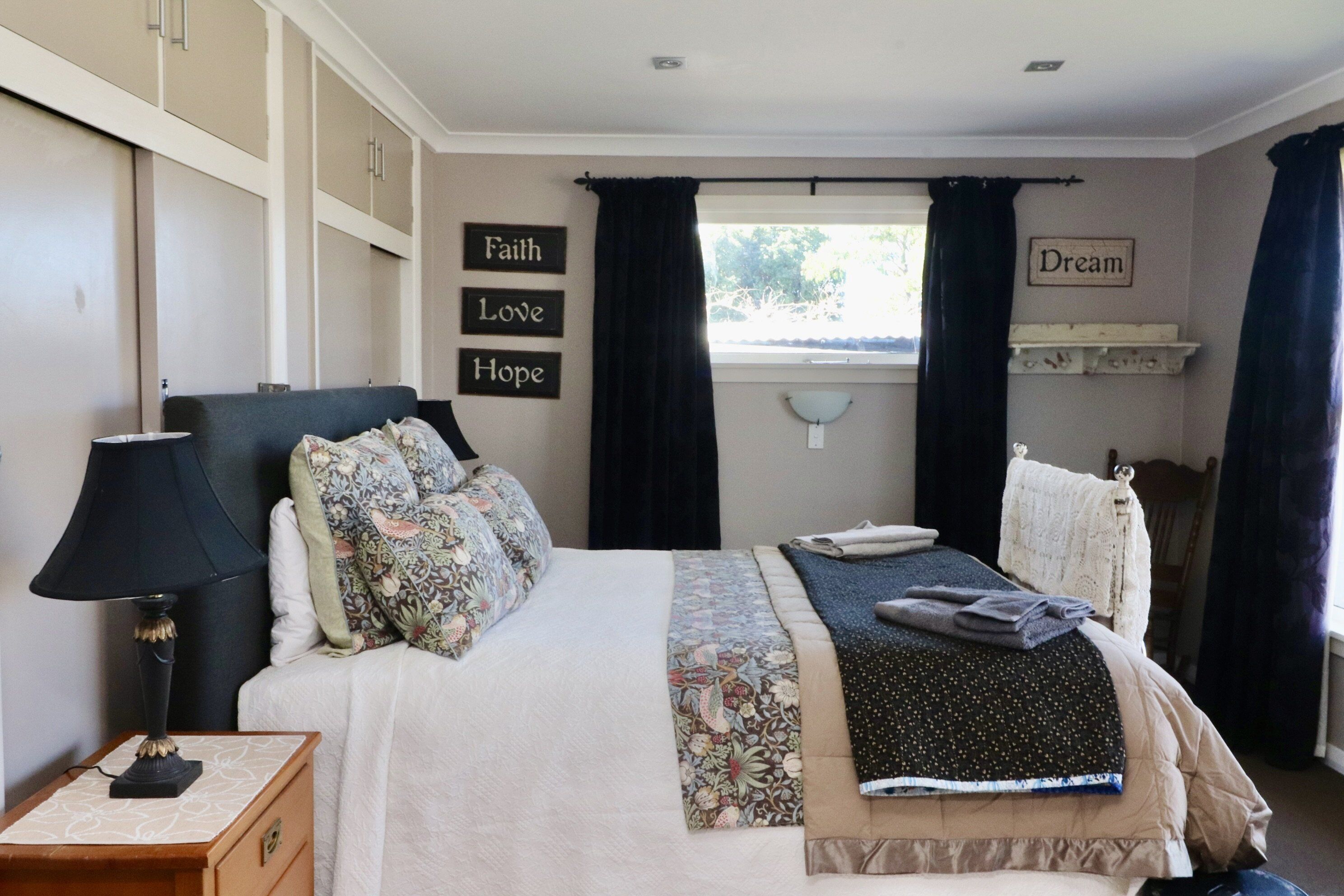 A bedroom with a bed, a nightstand, a lamp, a window with curtains, and motivational wall art.