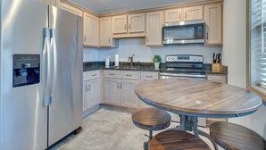Eine moderne Küche mit Edelstahlkühlschrank, Holzschränken, integriertem Mikrowellenherd und einem runden Esstisch mit Hockern.