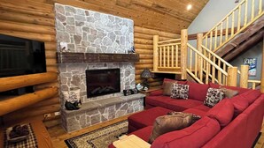 L’intérieur d’une cabane en rondins, avec une cheminée en pierre, un canapé rouge, un plancher en bois et un escalier.