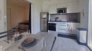 Una cocina moderna con armarios blancos, un refrigerador de acero inoxidable y un microondas. Hay un comedor con una mesa preparada para dos personas, incluyendo platos, vasos y cubiertos.