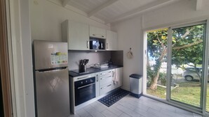 Una cocina moderna con armarios blancos, un refrigerador de acero inoxidable, un microondas y un lavamanos. Hay un bote de basura pequeño y una alfombra negra cerca de la puerta.