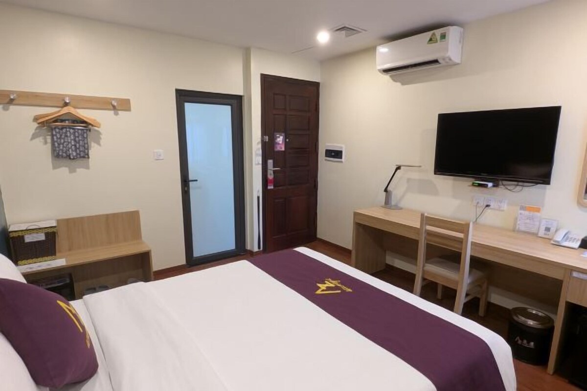 A hotel room with a bed, a desk, a television, and a door.