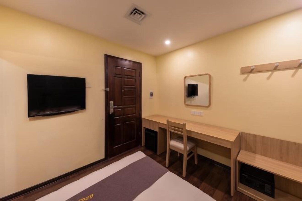 A room with a wooden door, a flat-screen TV mounted on the wall, a desk with a chair, and a mirror above the desk.