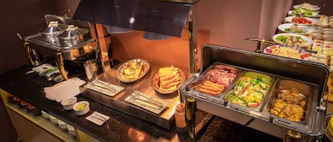 Un bufé con diversas opciones de comida, incluyendo perros calientes, ensaladas y carnes a la parrilla.