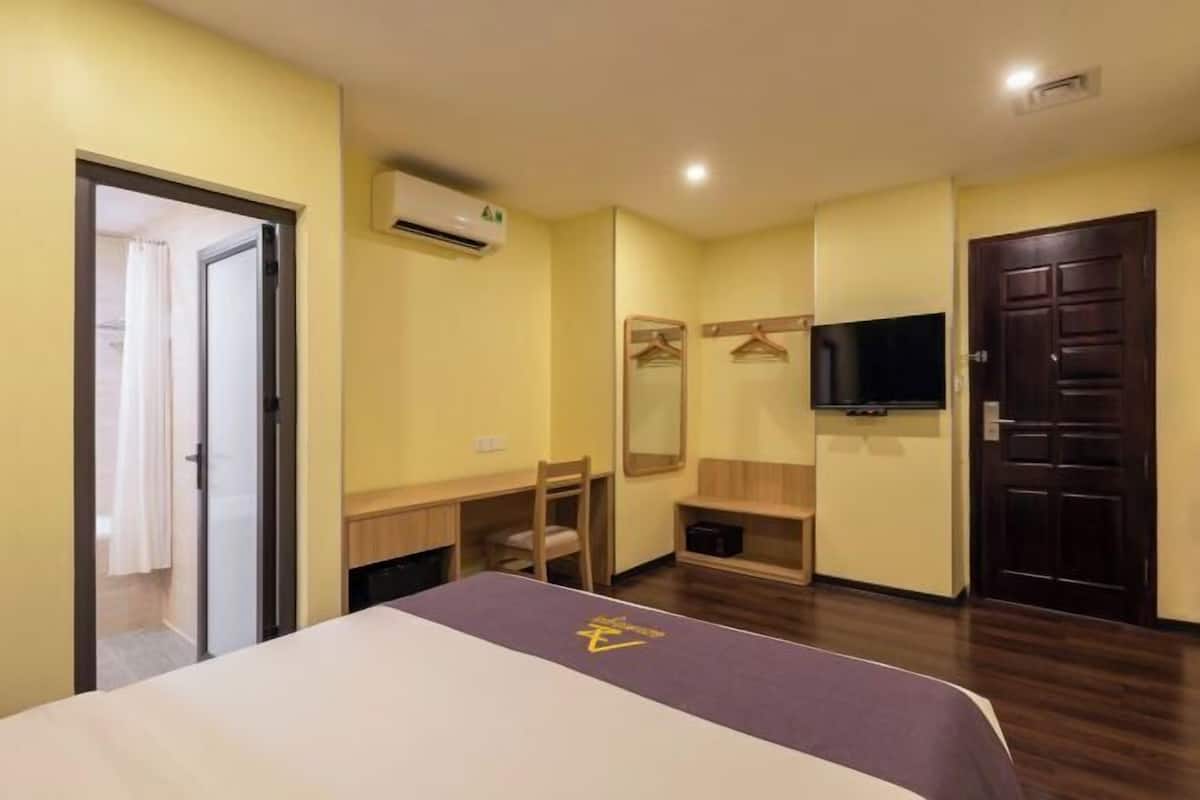 A hotel room with a bed, a desk, a chair, a TV, and a wardrobe.