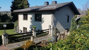 A white brick house with a sloped roof, a front porch, and a small garden area with a fire hydrant. - Ferienwohnung am Schöneberg Nähe Nürburgring (Heckenbach)
