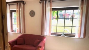 A room with a red sofa, a bed, a window with curtains, and a clock on the wall. - Ferienwohnung am Schöneberg Nähe Nürburgring (Heckenbach)