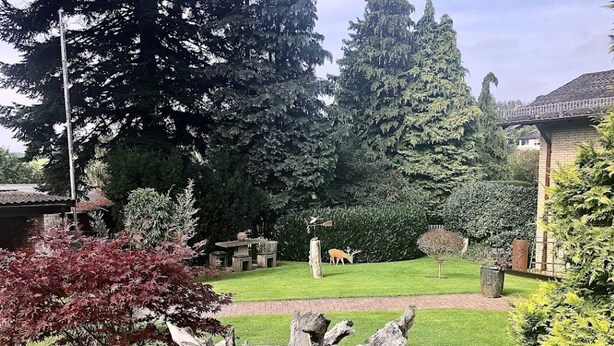 A garden with a deer, a wooden sculpture, and a brick pathway. - Ferienwohnung am Schöneberg Nähe Nürburgring (Heckenbach)
